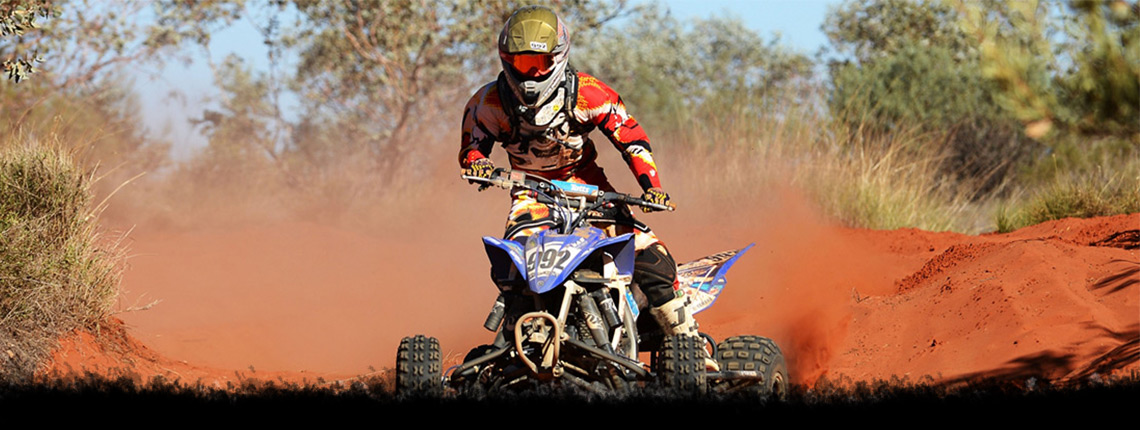 Person in full gear riding an ATV through a sandy trail
