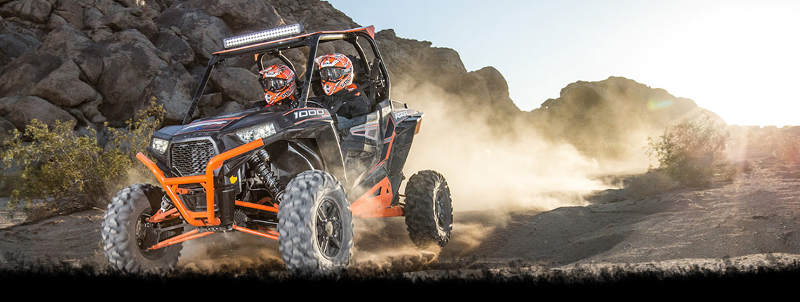 Two people riding in an orange ATV on rocky terrain on a mountain
